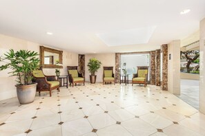 A spacious lobby with hexagonal patterned flooring, several chairs with green cushions, and large potted plants.