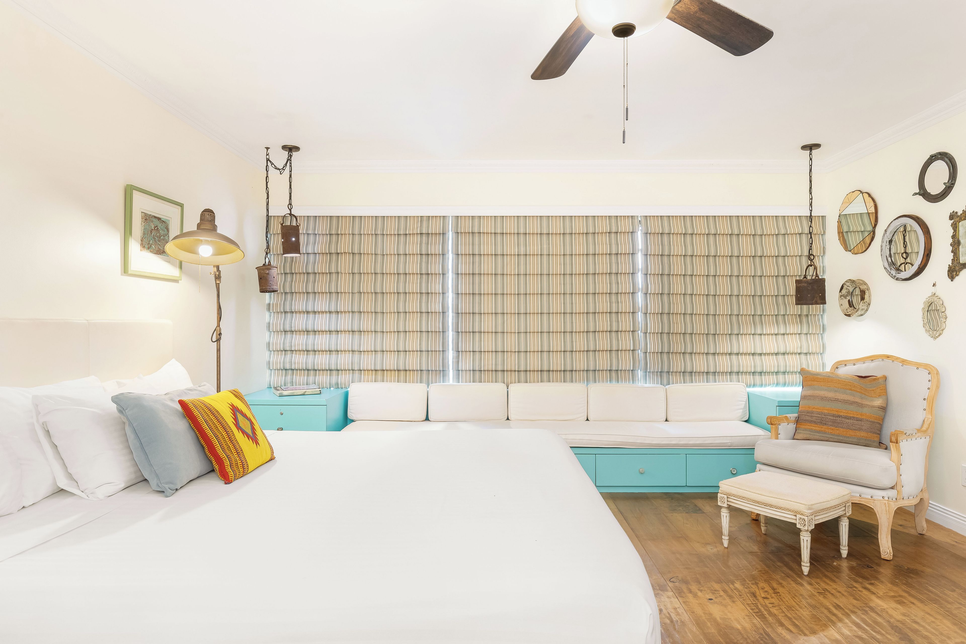A bedroom with a large bed, a sofa, a chair, and a ceiling fan.