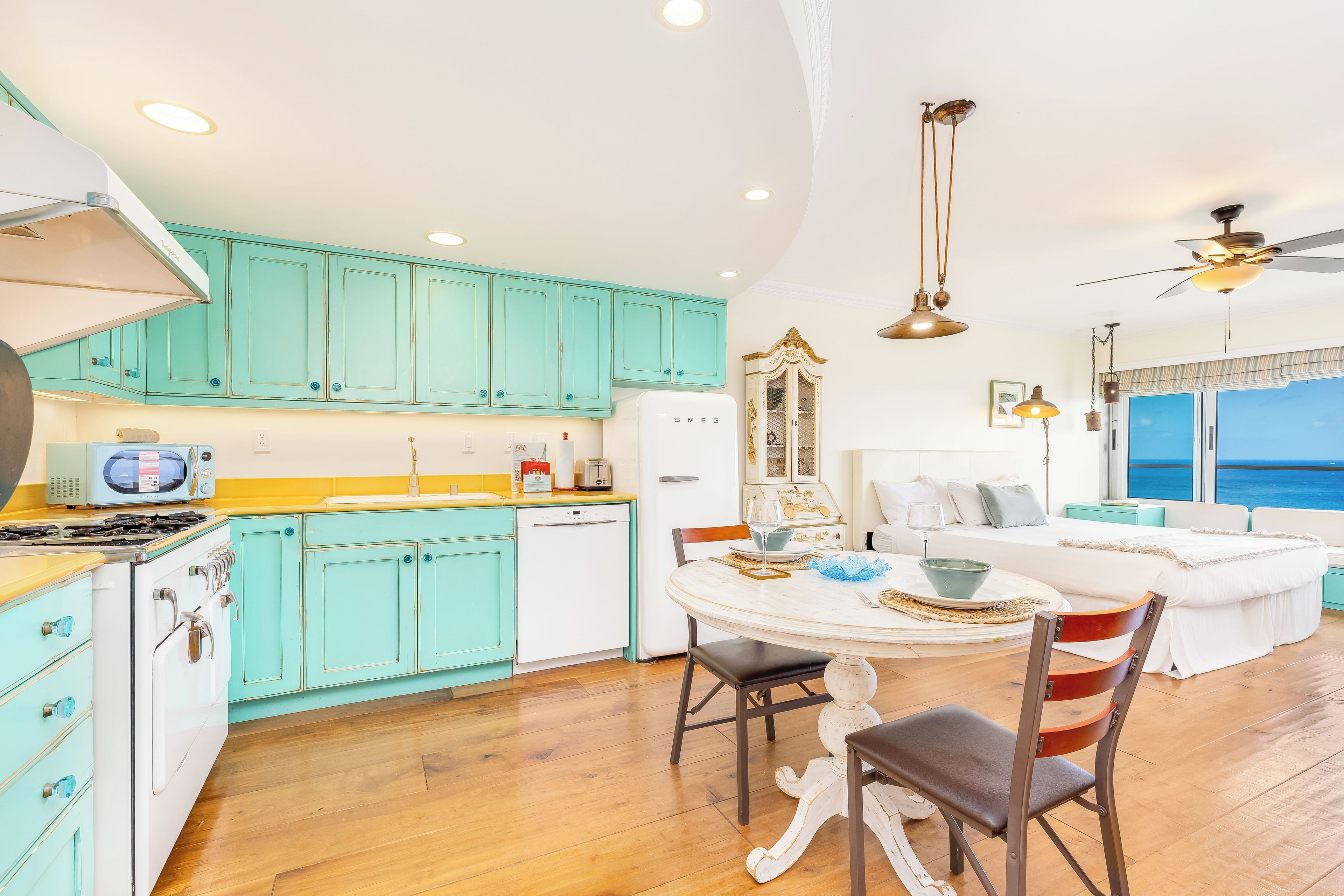 A kitchen with teal cabinets, a white refrigerator, and a dining area with a round table and chairs.