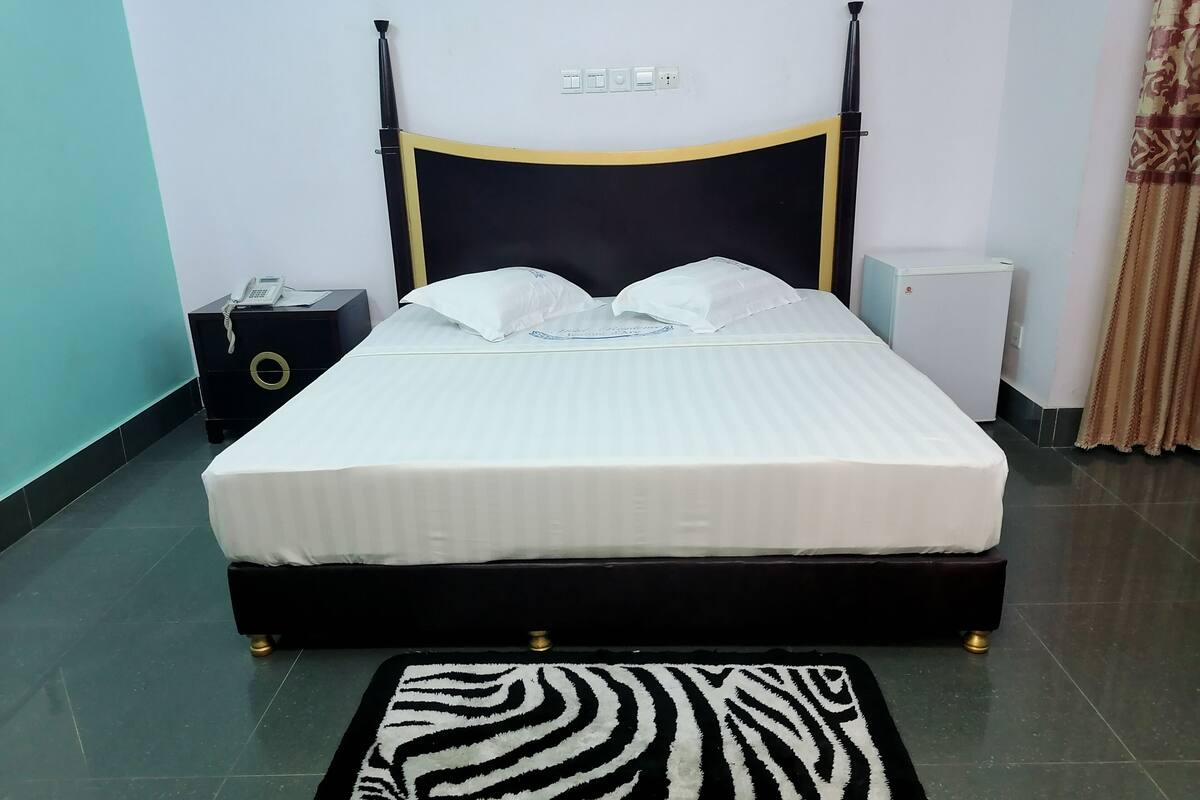 A neatly made bed with white bedding, a zebra-patterned rug, and a black and gold headboard.