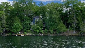 A lakeside cabin surrounded by dense forest, with a dock extending into the water. - A Cottage on a Private Island Big Rideau Lake (Perth)