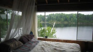 A bedroom with a large window offering a view of a lake and forest. - A Cottage on a Private Island Big Rideau Lake (Perth)