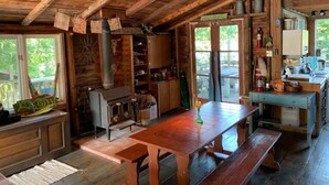 A rustic cabin interior with a wooden dining table, benches, a fireplace, and a kitchen area. - A Cottage on a Private Island Big Rideau Lake (Perth)