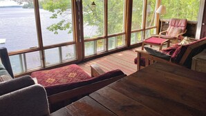 A wooden deck with a view of a lake, a cushioned seating area, and a table. - A Cottage on a Private Island Big Rideau Lake (Perth)