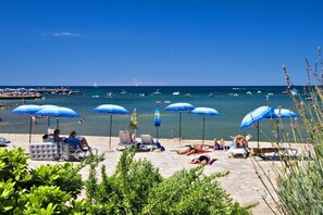 A beach with sun loungers and umbrellas, a clear blue sky, and boats in the water. - Adriamar Mobile Homes in Camping Park Umag  / Adriamar 2439 Park Umag (Karigador)