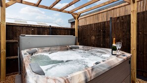 Un jacuzzi con una pérgola de madera, una botella de champán y dos copas al borde.
