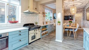 Una cocina moderna con paredes de azulejos blancos, estufa integrada y un comedor con mesa y sillas de madera.