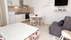 Ein kompakter Wohnbereich mit Küchenzeile, Essplatz, Sofa und an der Wand montiertem Fernseher.