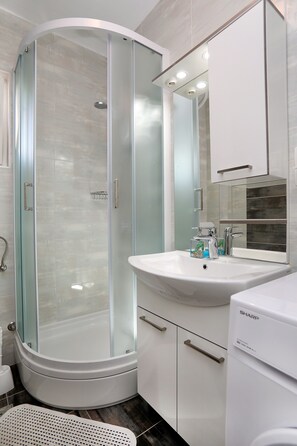 Un bagno moderno con doccia vetrata, lavandino bianco e specchio soprastante.