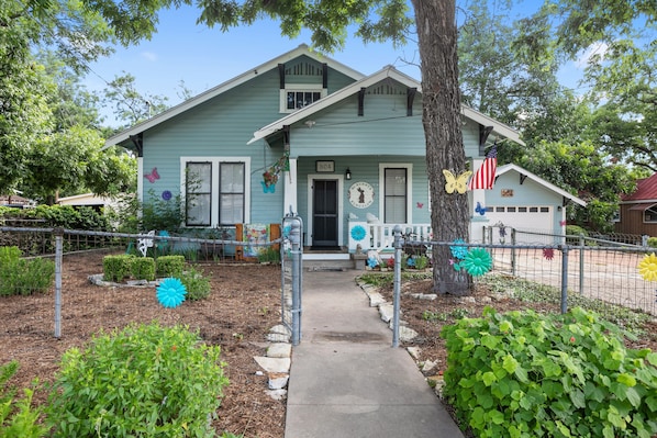 A light blue house with a front porch, a mailbox, and a small garden with decorative flowers.