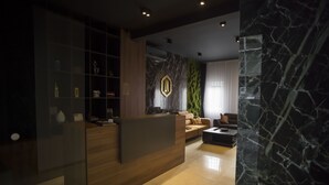 Un área de recepción moderna con un mostrador de madera, una pared texturizada de color verde y un suelo de mármol.