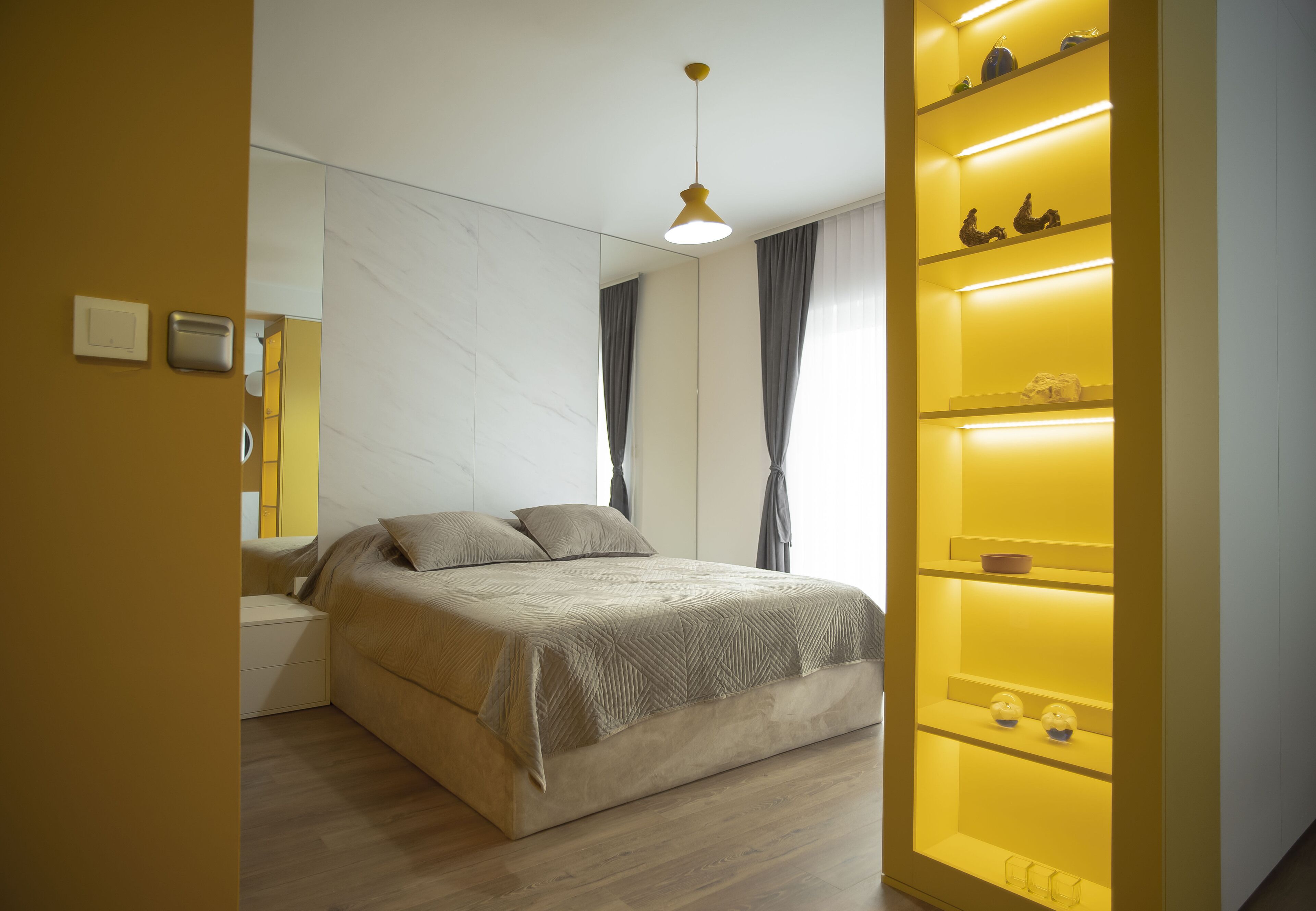 A modern bedroom with a bed, bedside tables, a built-in shelf with decorative items, and a pendant light.