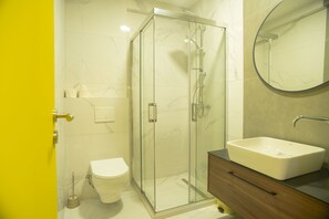 A bathroom with a glass-enclosed shower, a white toilet, and a sink with a wooden vanity. - Lux Apartments (Pristina)