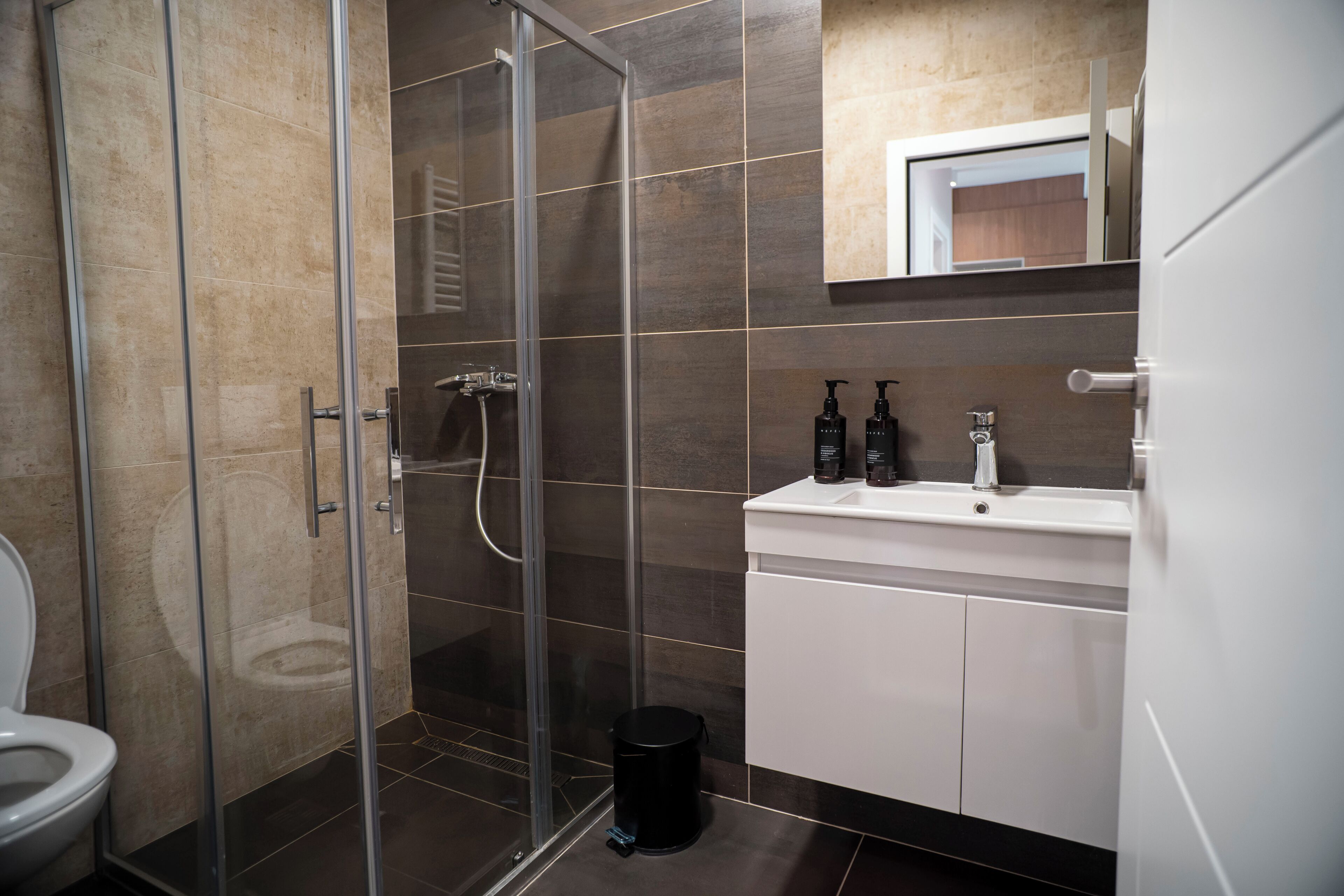 Une salle de bain moderne avec une douche à parois de verre, un lavabo blanc et un miroir au-dessus du lavabo.