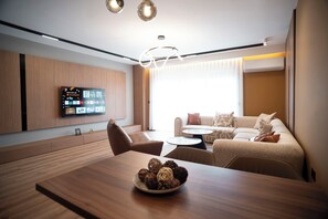 A modern living room with a wooden dining table, a sofa, and a television mounted on the wall. - Lux Apartments (Pristina)