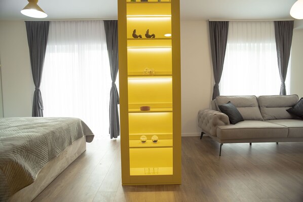 A modern hotel room with a bed, a sofa, and a yellow accent wall with shelves.