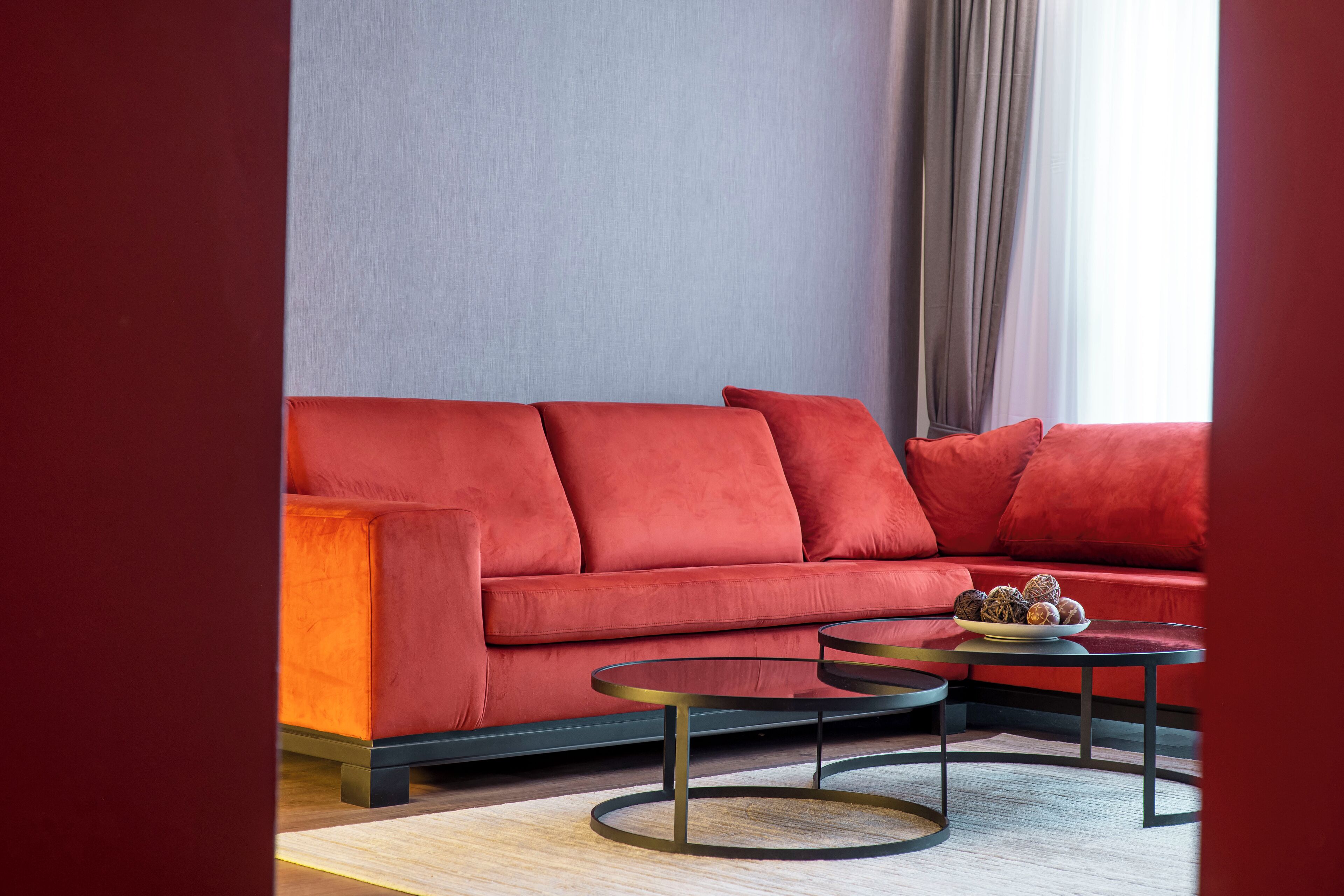 Una sala de estar moderna con un sofá rojo, dos mesas redondas de centro y un plato de aperitivos sobre una de ellas.