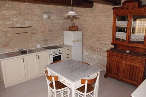 A kitchen with a marble countertop, white cabinets, a white refrigerator, and a wooden cabinet with glass doors.