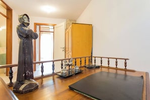 Une pièce avec un plancher en bois, une statue, une petite table avec un plateau, une porte et une rampe d’escalier.