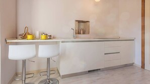 A modern kitchen with a central island, bar stools, a hanging light fixture, and a small window.