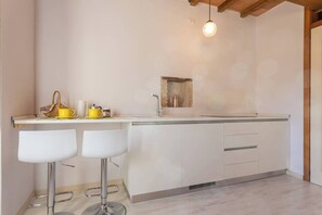 A modern kitchen with a central island, bar stools, a hanging light fixture, and a small window.