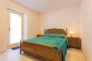Une chambre à coucher avec un lit en bois, deux tables de chevet avec des lampes, une porte et une fenêtre.