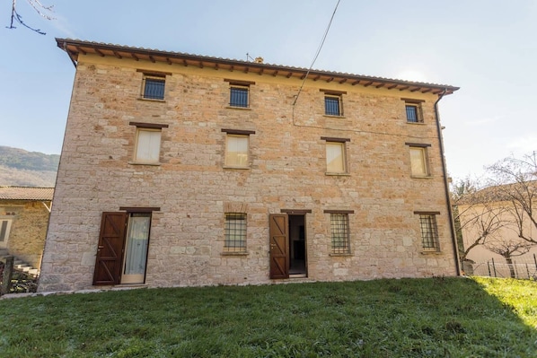A stone building with multiple windows and doors, surrounded by a grassy area.