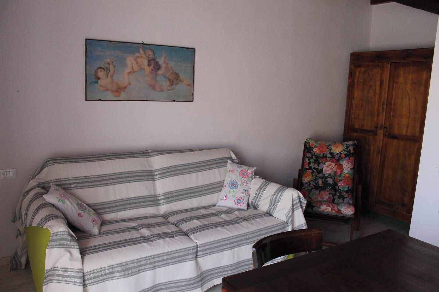 A room with a striped sofa, a floral chair, a wooden cabinet, and a painting on the wall.