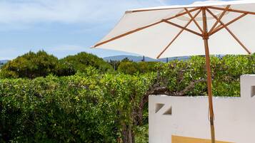 Enjoy al fresco dining on the patio, surrounded by lush greenery and shaded by a large umbrella.