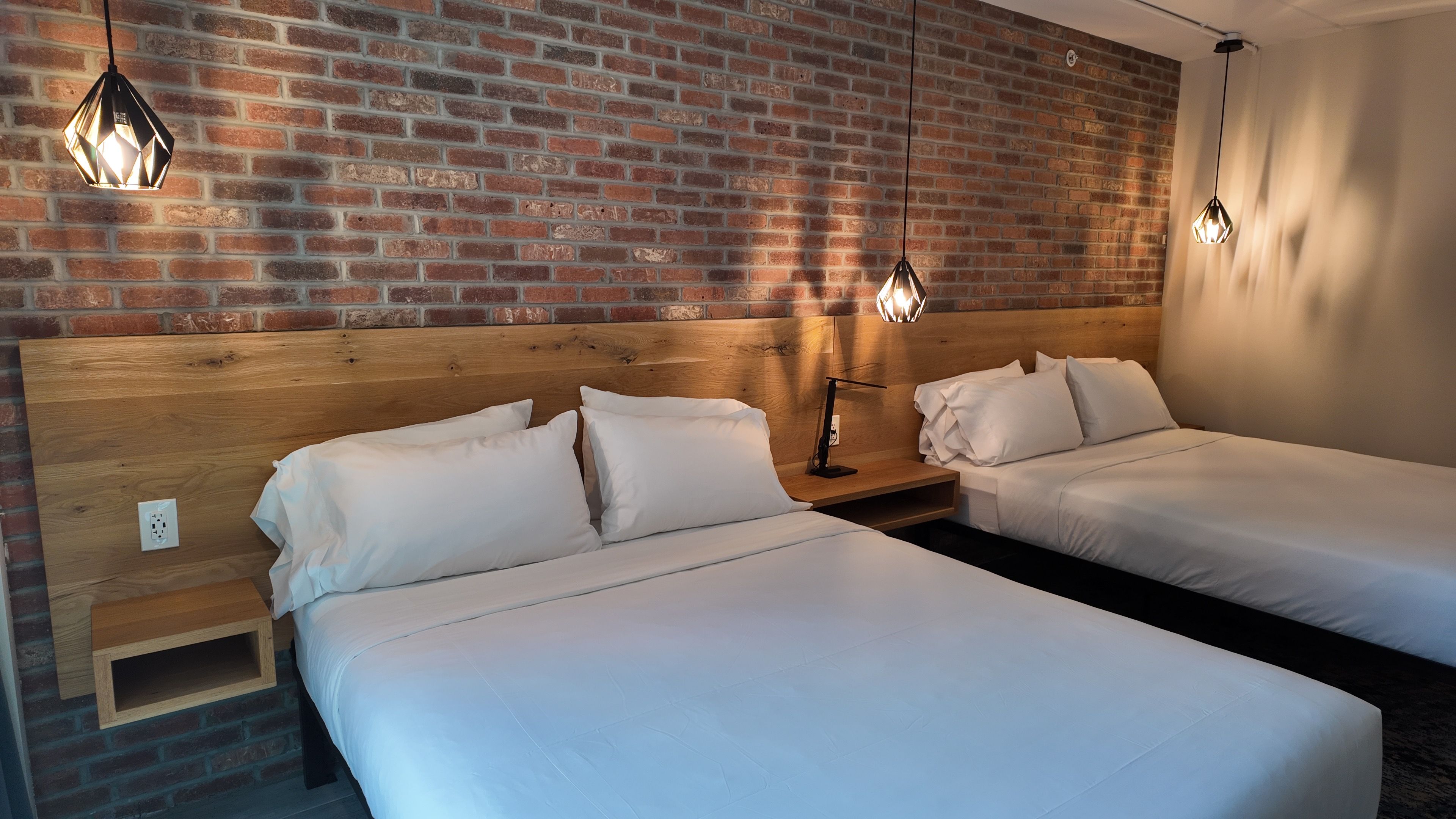 Habitació d'hotel amb dos llits, una paret de maó i llums penjants.