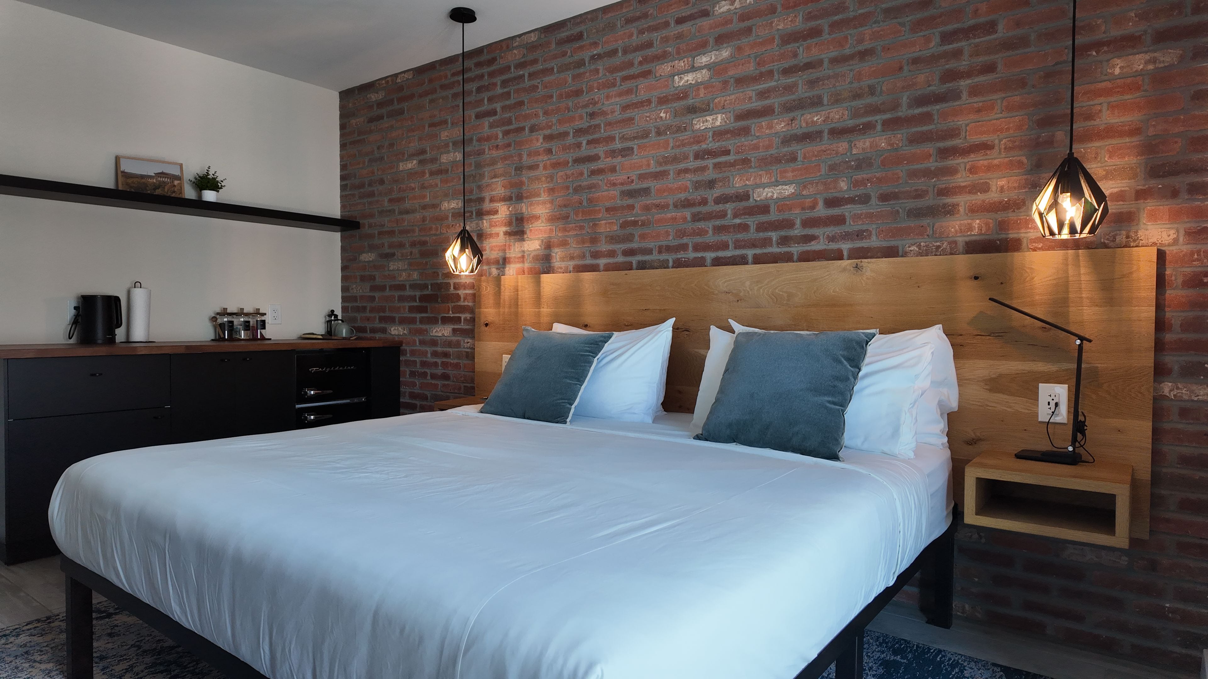 Un dormitorio moderno con pared de ladrillo, cabecero de madera, cama con ropa de cama blanca y dos lámparas de noche.