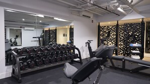 A gym with exercise equipment, a mirror, and a wall-mounted dumbbell rack. - The Maj Hotel (Philadelphia)