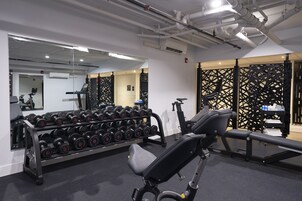 Un gimnasio con equipamiento de ejercicio, un espejo y un estante de mancuernas en la pared.