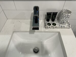 A bathroom sink with a chrome faucet, a soap dispenser, and a soap dish with two bottles. - The Maj Hotel (Philadelphia)