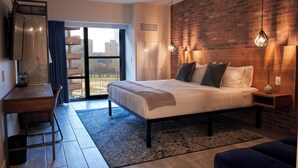 A modern bedroom with a large bed, a desk, and a view through a glass door. - The Maj Hotel (Philadelphia)