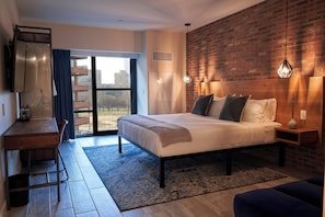 A modern bedroom with a large bed, a desk, and a view through a glass door. - The Maj Hotel (Philadelphia)