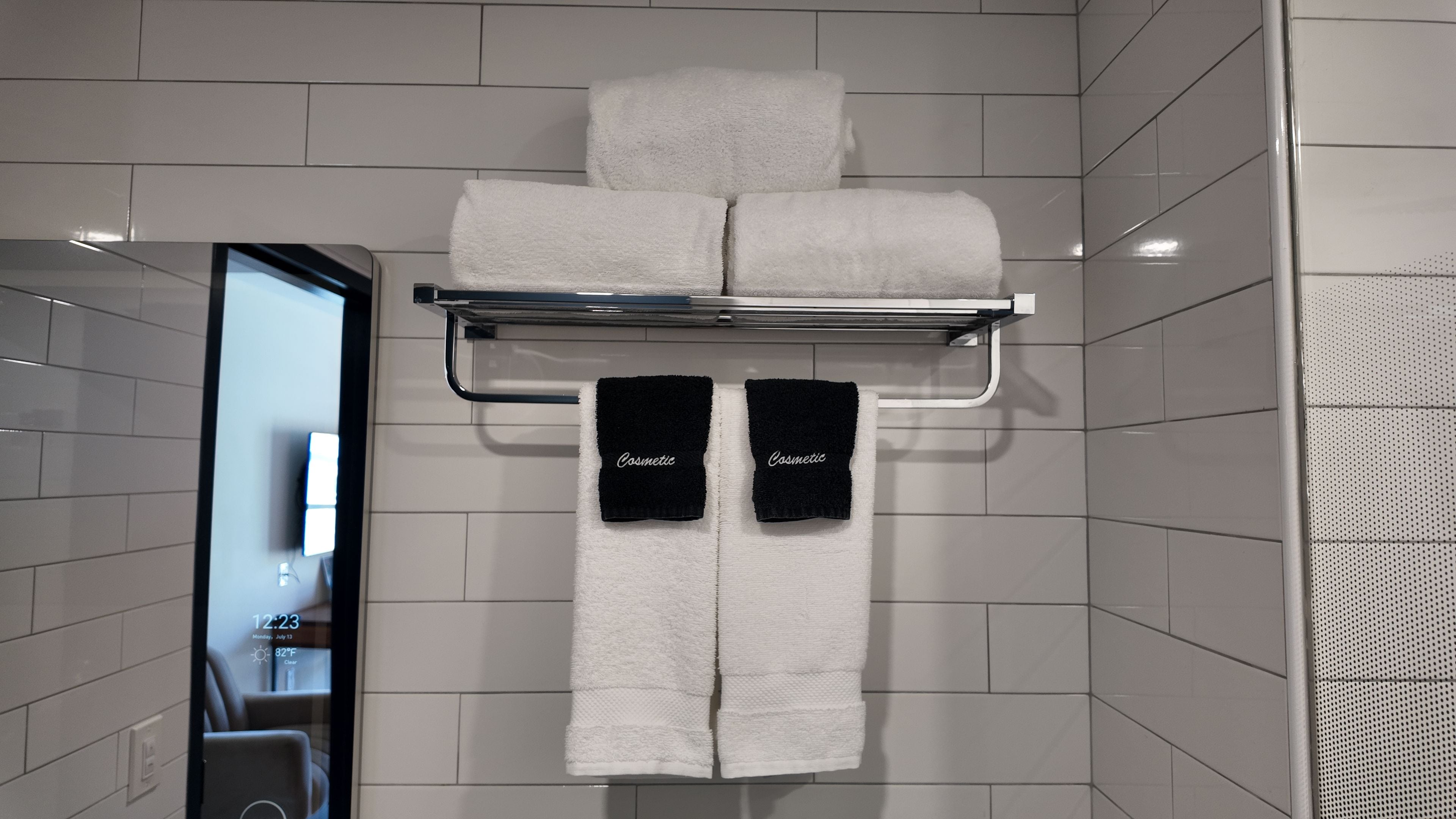 Casa de banho com suporte de toalhas contendo duas toalhas brancas e duas toalhas pretas com a palavra 'Cosmetic' escrita nelas.