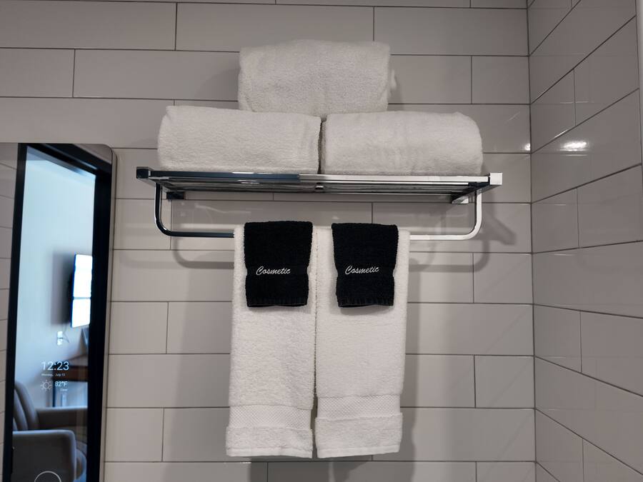 A bathroom with a towel rack holding two white towels and two black towels with 'Cosmetic' written on them.