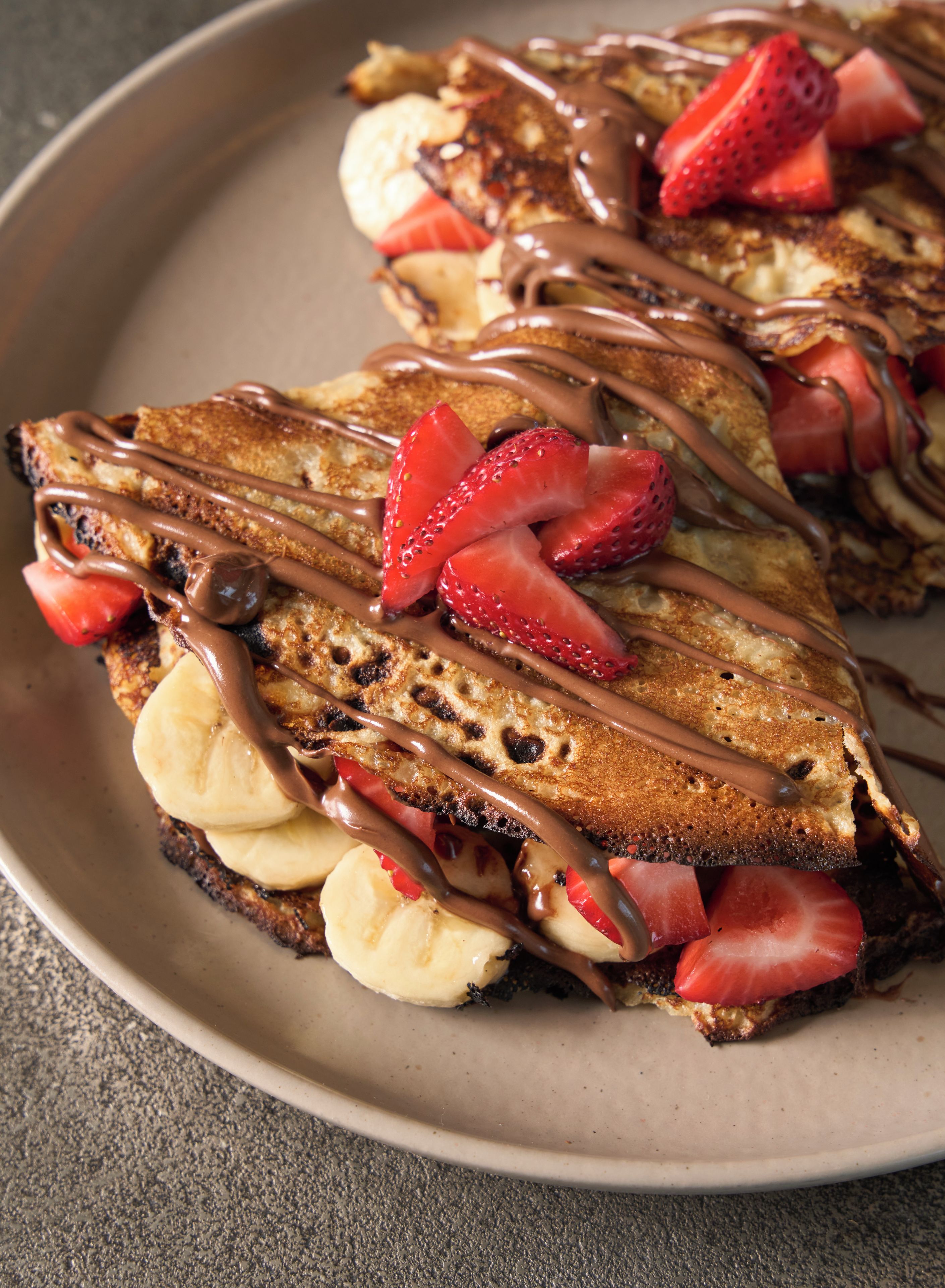 A plate of French toast with strawberries and bananas, topped with chocolate sauce.