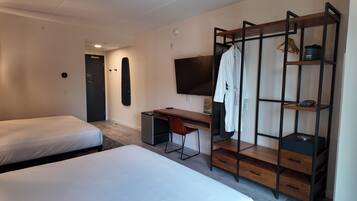 A hotel room with two beds, a desk with a chair, a TV, a wardrobe, and a small kitchenette.