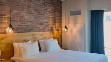A hotel room with a brick wall, a bed with white bedding, a wooden headboard, a nightstand, and two pendant lights.
