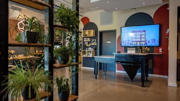 A modern interior with a reception desk, a large flat-screen TV displaying a building image, and various plants.