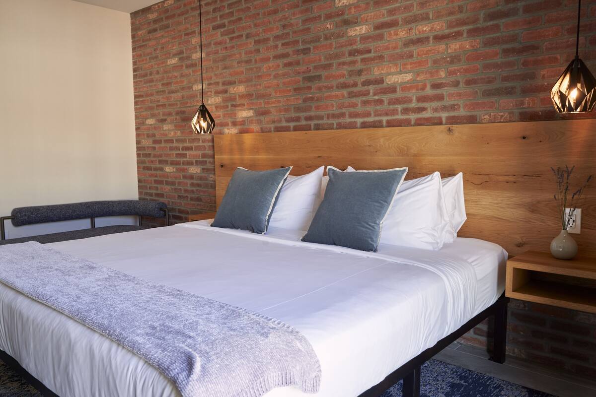 A modern bedroom with a large bed, a wooden headboard, and a brick wall.