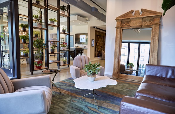 A modern living room with a large mirror, leather sofas, a coffee table with a plant, and a bookshelf filled with books and plants. - The Maj Hotel (Philadelphia)