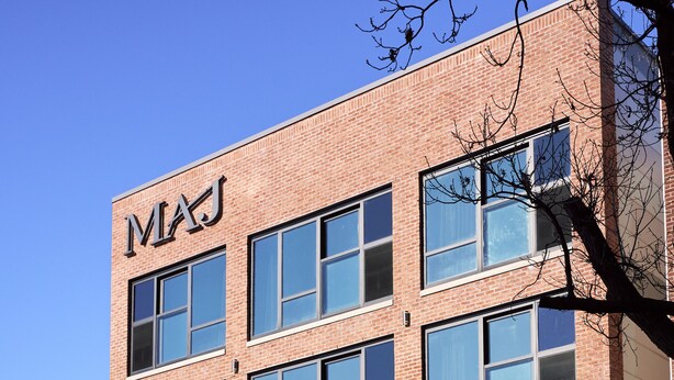 Un edificio de varios pisos con un llamativo letrero 'MAJ' en la fachada, que presenta grandes ventanales y revestimiento de ladrillo.