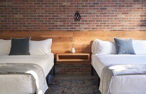 A hotel room with two beds, a wooden headboard, a brick wall, and a small nightstand with a vase. - The Maj Hotel (Philadelphia)