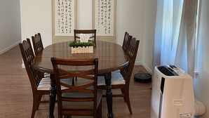 Une salle à manger avec une table ronde en bois, six chaises, deux rouleaux verticaux ornés de calligraphie, une petite plante sur la table et un appareil électroménager blanc sur le côté droit.