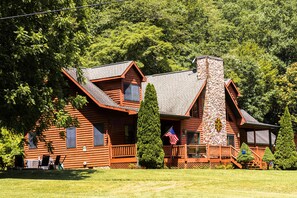 Une cabane en rondins avec une cheminée en pierre, une terrasse en bois et un drapeau américain.