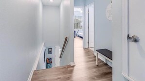 A narrow hallway with light blue walls and wooden flooring, leading to a room with a bed and a window. - G & J Paradise (Rockport)