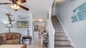 A living room with a sofa, coffee table, and a staircase leading to a kitchen area. - G & J Paradise (Rockport)